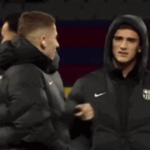 a man in a black jacket with a hood is standing next to another man in a black jacket .