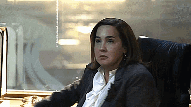 a woman in a suit sits in a chair in front of a window with the letter k on it