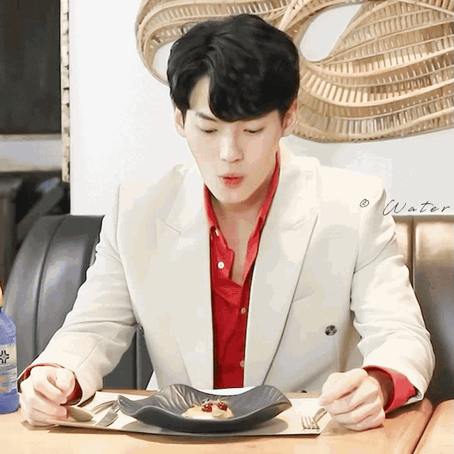 a man in a white jacket and red shirt is sitting at a table with a plate of food