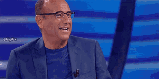 a man wearing glasses and a blue suit is smiling and clapping his hands