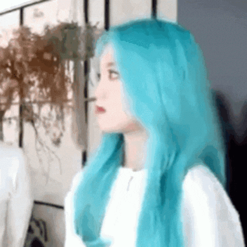 a girl with blue hair is wearing a white shirt and looking at the camera .