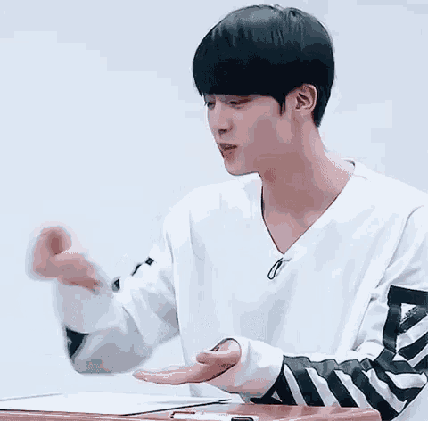 a young man with black hair and a white shirt is sitting at a table with his mouth open .