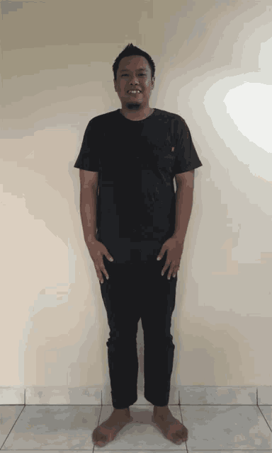 a man wearing a black shirt and black pants is standing with his hands on his hips