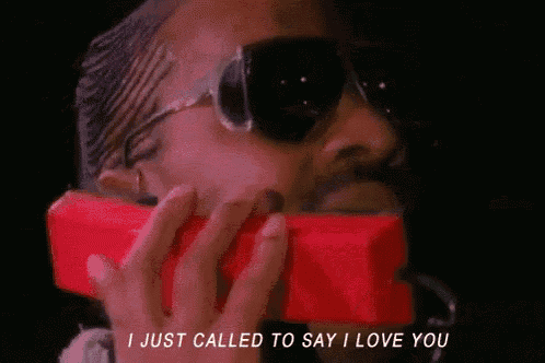 a man wearing sunglasses is talking on a red telephone .