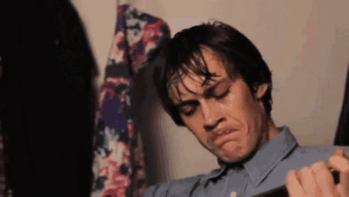 a man in a blue shirt is making a funny face while looking at his phone .