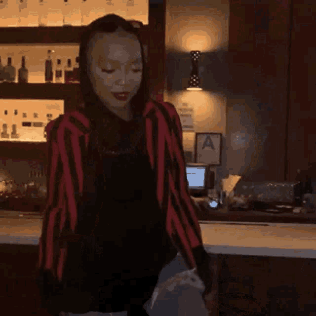 a woman in a red and black striped jacket is standing in front of a bar holding a bag .