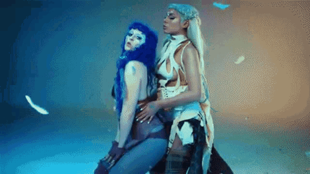 two women with blue hair and white hair are standing next to each other in a dark room .