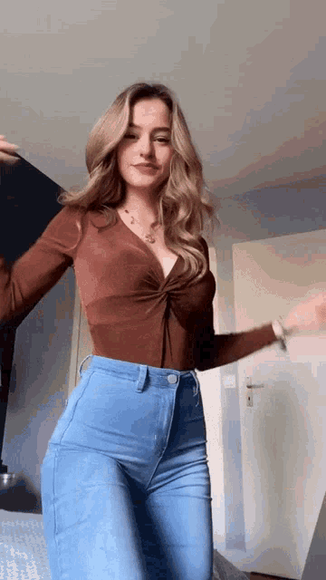 a woman in a brown top and blue jeans is standing in front of a door