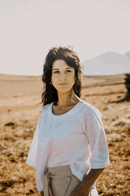 a woman stands in a field wearing a white shirt