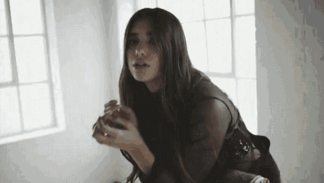 a woman with long hair is sitting in front of a window