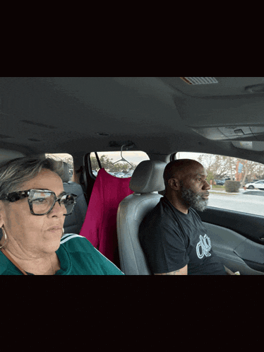 a man and a woman are sitting in a car and the man is wearing a black shirt with the letter o on the front