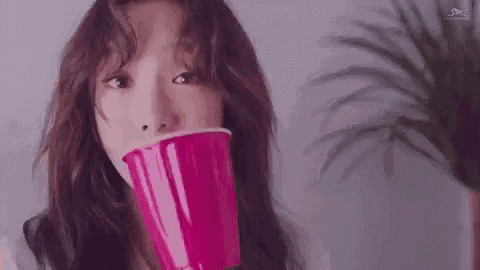a woman is drinking from a pink cup with her mouth open .
