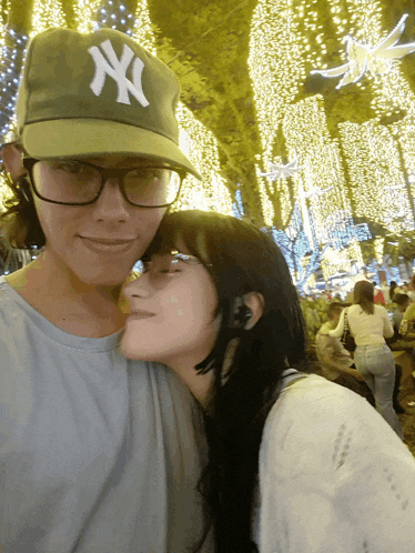 a man wearing a ny hat and glasses is kissing a woman on the cheek
