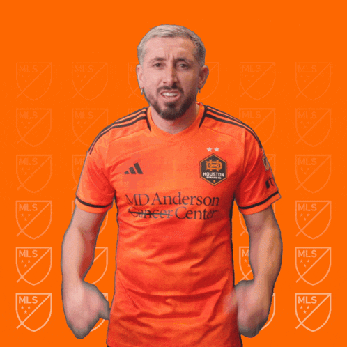 a man wearing an orange shirt that says manderson soccer center holds his fist in the air