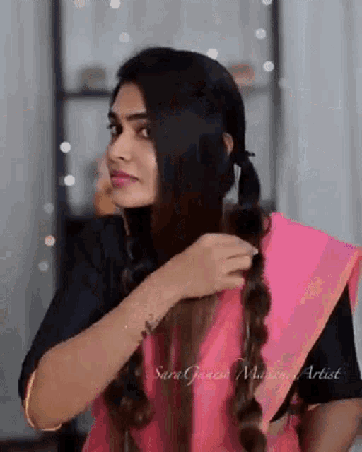 a woman is braiding her hair in a pink saree .