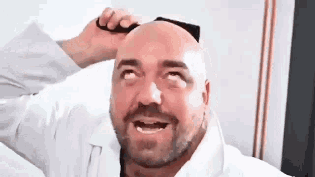 a bald man with a beard is smiling while brushing his hair .
