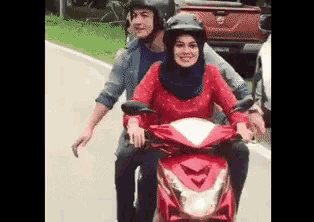 a man and a woman are riding a red scooter down a road .