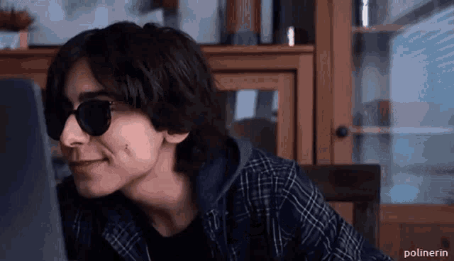 a young man wearing sunglasses and a plaid shirt is sitting in front of a computer .
