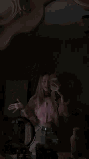 a woman in a pink shirt is taking a selfie in the dark and making a peace sign .