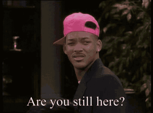 a man wearing a pink hat and a suit says " are you still here "