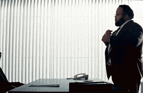 a man in a suit and tie is standing in front of a table with a phone on it .