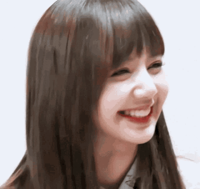 a close up of a woman 's face with long brown hair and bangs smiling .