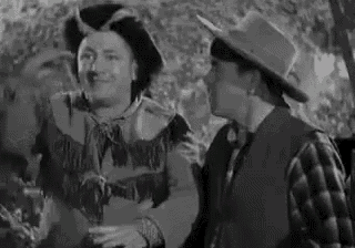 two men are standing next to each other in a black and white photo . one is wearing a cowboy hat .