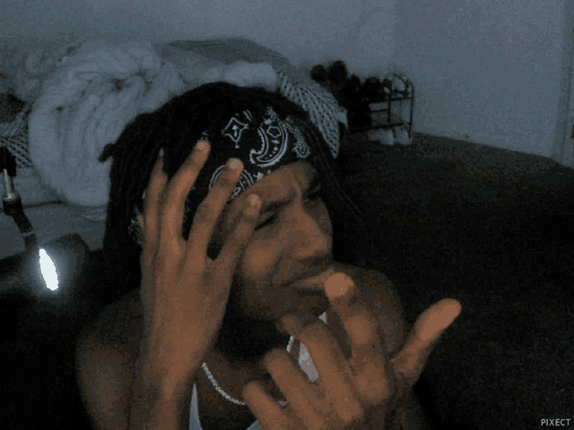 a man with dreadlocks wearing a bandana and a necklace is giving the middle finger