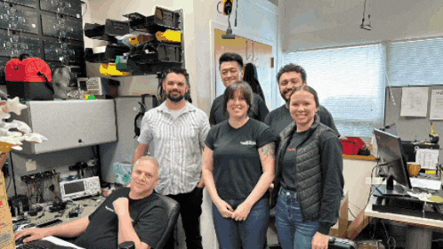 a group of people posing for a picture in an office with a man sitting at a desk