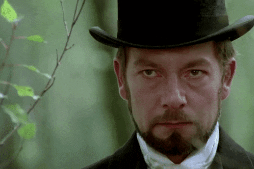a man with a beard wearing a top hat looks at the camera