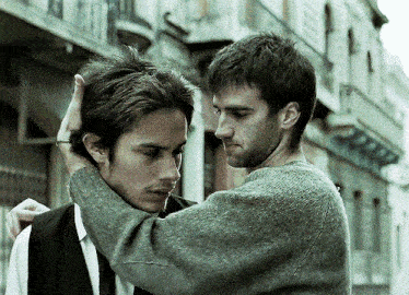 a man adjusts another man 's hair while standing in front of a building