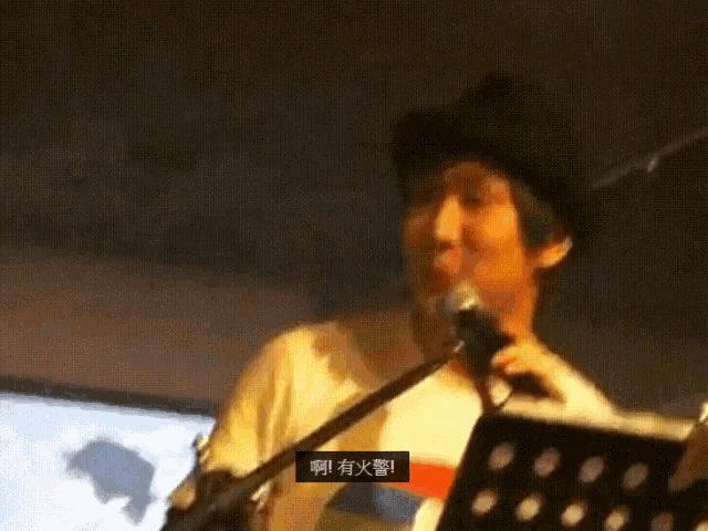 a man singing into a microphone with chinese characters on the screen behind him