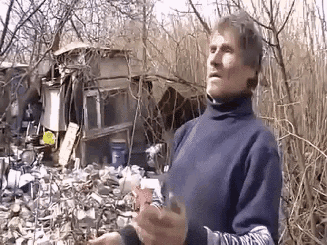 a man in a blue sweater stands in front of a pile of trash