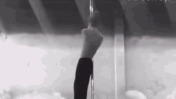 a black and white photo of a woman pole dancing in a room .