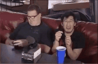 two men are sitting on a couch playing a video game with a blue cup in front of them