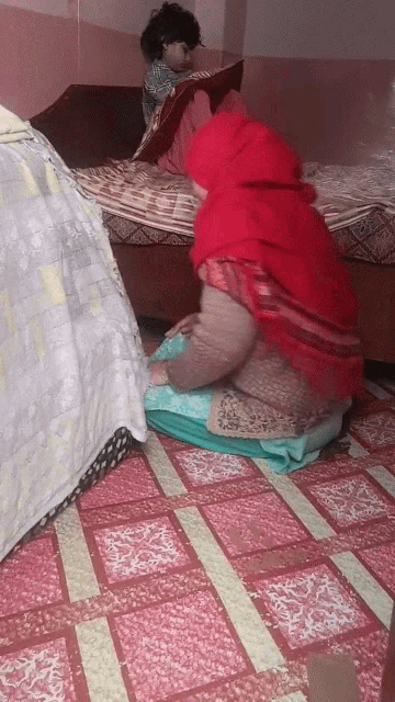 a woman in a red head scarf sits on the floor next to a child