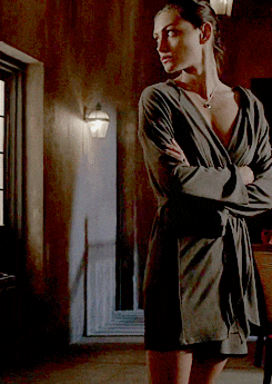 a woman in a robe stands with her arms crossed in front of a window