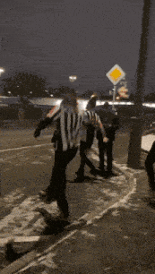 a group of people walking down a street at night with a yellow sign in the background