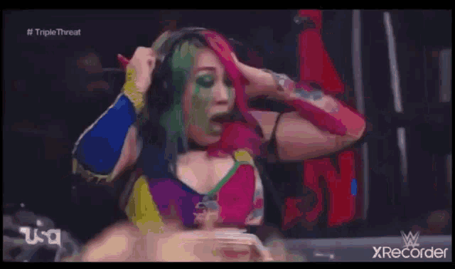 a woman with green hair is sitting in a chair in a wrestling ring on a television screen .