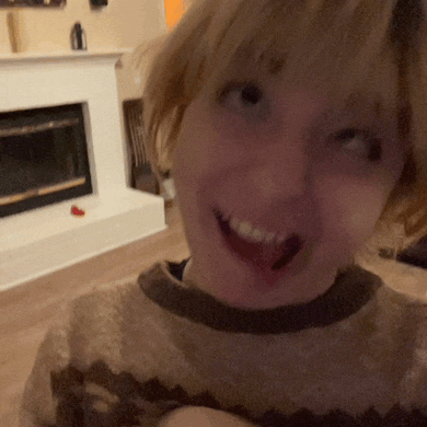 a woman wearing a brown and black sweater smiles in front of a fireplace