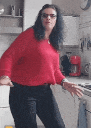 a woman wearing glasses and a red sweater is dancing in a kitchen .