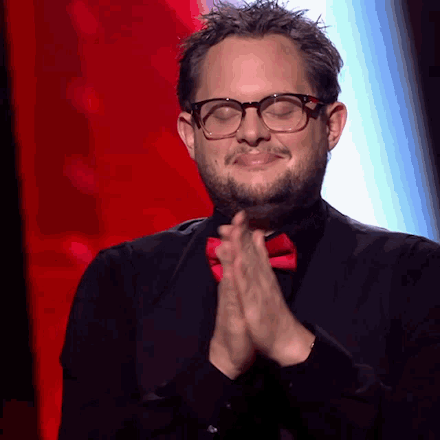 a man wearing glasses and a red bow tie holds his hands together