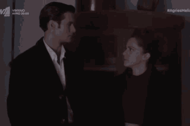 a man and a woman are looking at each other in a dark room with the words agriesmeli on the bottom