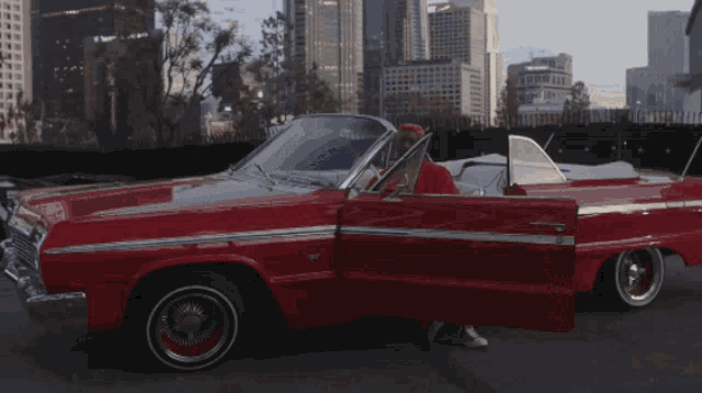 a red car with the door open is parked in front of a city