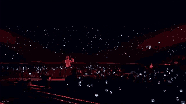 a man singing into a microphone in front of a crowd that is lit up with their phones
