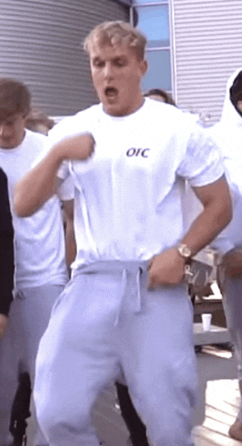 a man in a white t-shirt and grey sweatpants is dancing in front of a crowd .