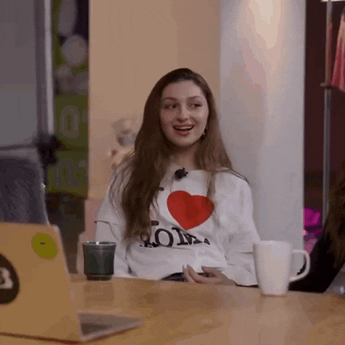 a woman is sitting at a table wearing a white shirt that says i love you