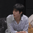 a man in a white shirt is sitting on a couch talking to a cat .
