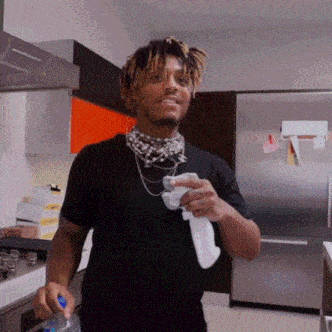 a man in a black shirt is standing in a kitchen holding a bottle of water and a towel