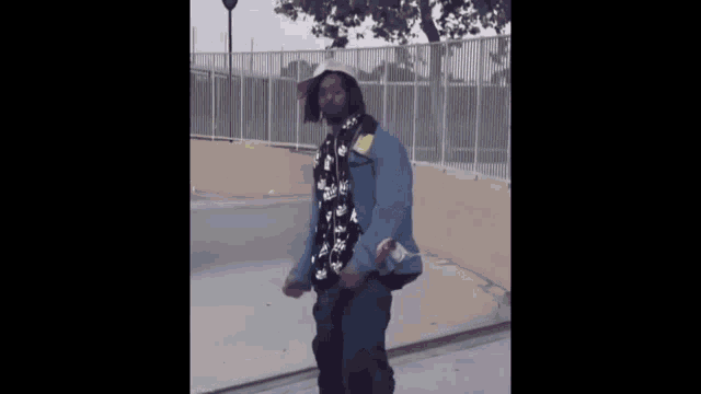 a man wearing a hat and a denim jacket is standing on a sidewalk